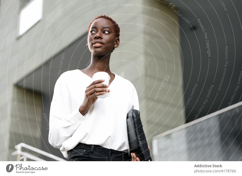 Fröhliche ethnische Geschäftsfrau mit Kaffee zum Mitnehmen auf der Straße Imbissbude positiv elegant modern urban trinken heiter Stil jung schwarz