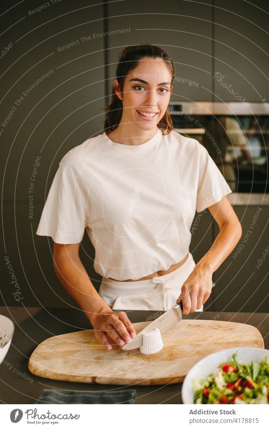 Lächelnde Frau Schneiden von Käse für Salat in der Küche Feta geschnitten Salatbeilage vorbereiten Koch Gemüse lecker heimwärts selbstgemacht Messer Gesundheit