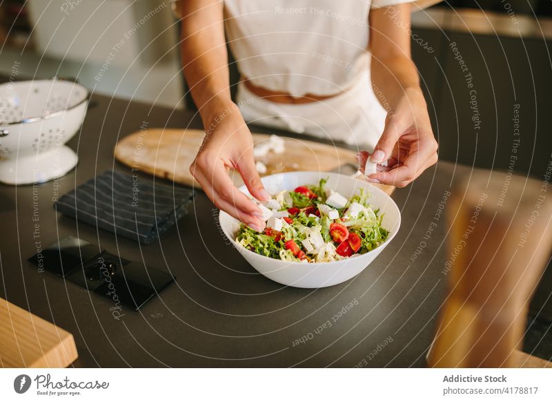 Crop Frau Kochen Gemüsesalat zu Hause Salatbeilage Käse Feta hinzufügen vorbereiten Mittagessen gesunde Ernährung frisch Bestandteil Gesundheit Küche