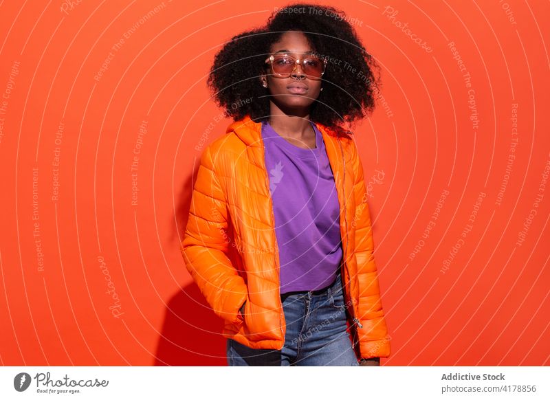 Stilvolle schwarze Frau mit Afrofrisur lebhaft lässig trendy farbenfroh Sonnenbrille Frisur Zeitgenosse hell schick Jacke cool Mode purpur orange Accessoire