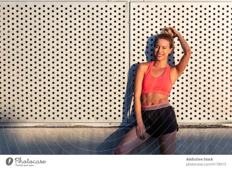 Fröhliche Sportlerin steht in der Nähe eines Gebäudes auf der Straße Läufer Großstadt Athlet schlank passen heiter Sommer sonnig Frau stehen Sportbekleidung