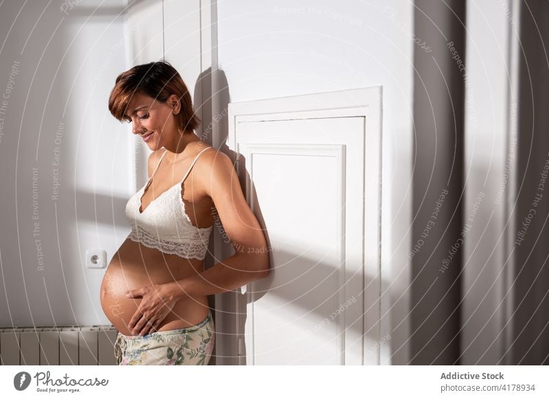 Zarte schwangere Frau, die ihren Bauch berührt berühren Magen BH mütterlich Schwangerschaft filigran erwarten pränatal Angebot heiter Pflege Dessous Lächeln