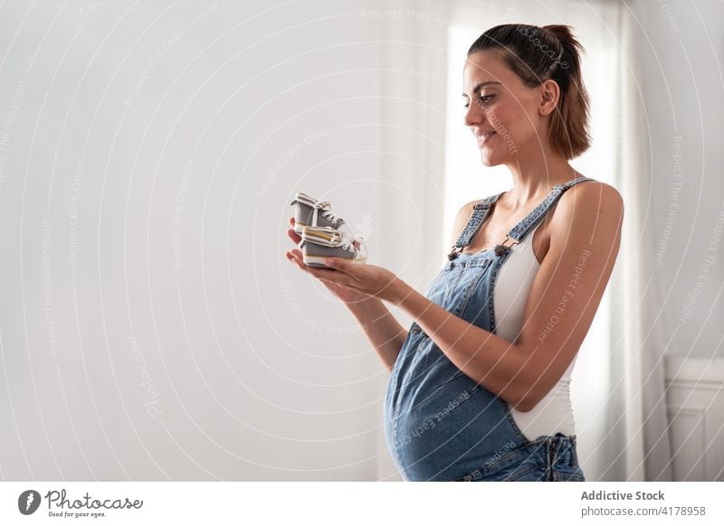 Schwangere Frau stehend mit winzigen Babystiefeln schwanger Stiefel Schuh Schnüffler Bauch Schwangerschaft Kleiderschrank heimwärts klein mütterlich erwarten