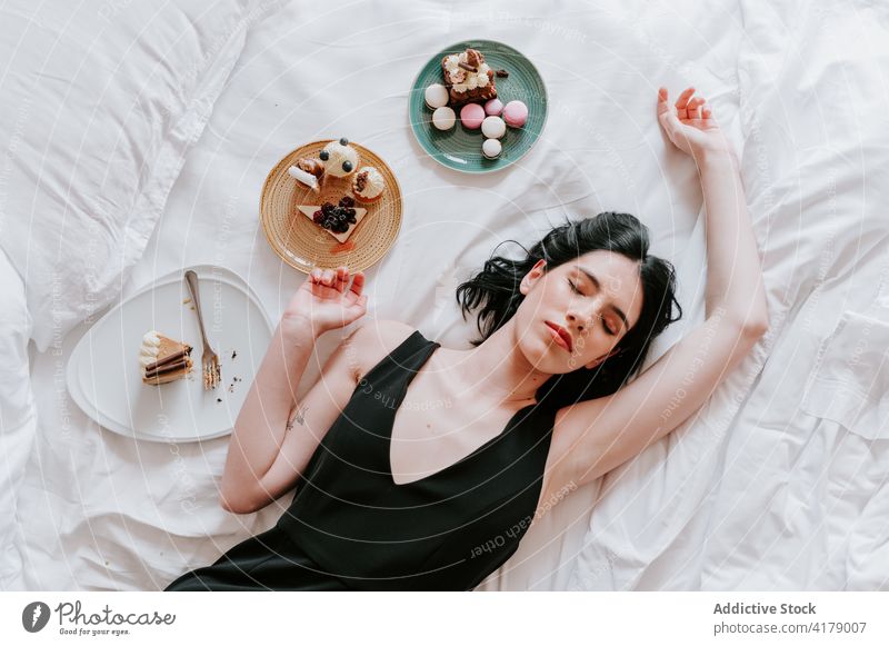 Friedliche Frau auf dem Bett liegend mit verschiedenen Nachspeisen Dessert Hotel Reichtum dienen Kulisse süß sortiert geschmackvoll Wochenende lecker sorgenfrei
