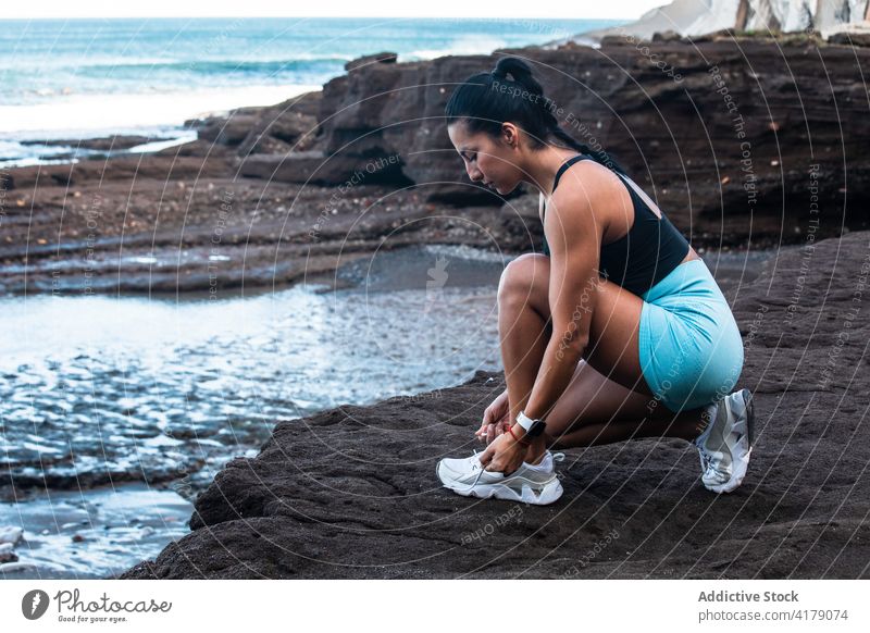 Junge Sportlerin beim Binden der Schnürsenkel vor dem Training Krawatte Schuhbänder Turnschuh Schuhe vorbereiten Meeresufer Seeküste Frau ethnisch