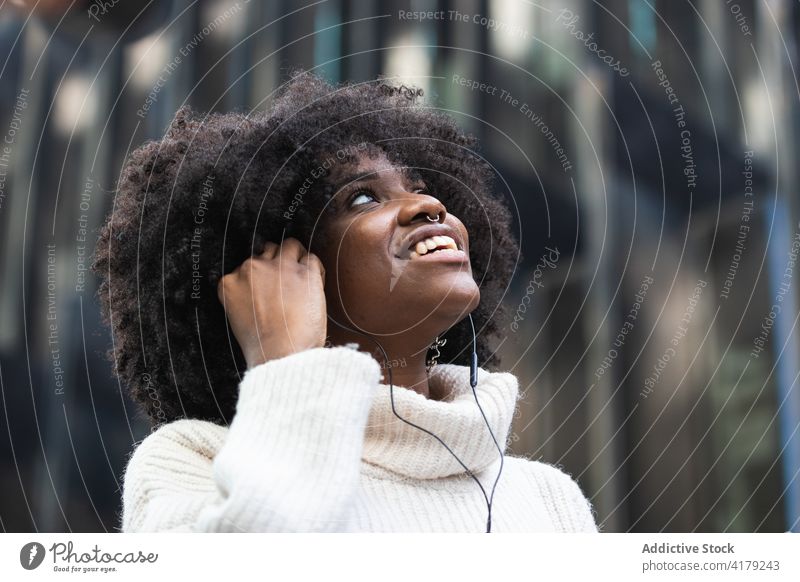 Glückliche schwarze Frau mit Kopfhörern, die auf ihrem Smartphone Musik hört zuhören Optimist heiter Kälte genießen jung Spaß haben positiv Afroamerikaner