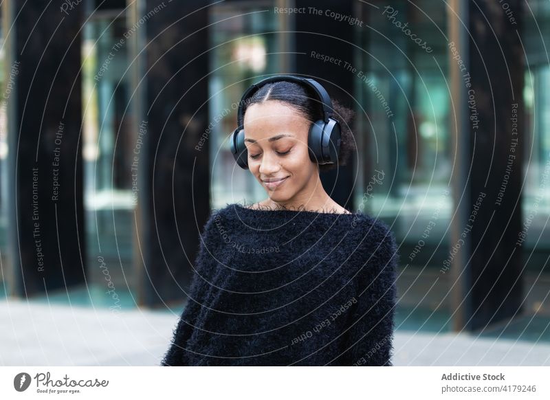 Schwarze Frau beim Musikhören auf der Straße zuhören Kopfhörer Kälte genießen jung Drahtlos positiv Afroamerikaner schwarz ethnisch Schüler Jugendlicher