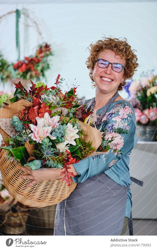 Erfreute Frau mit Blumenstrauß im Geschäft Blumenhändler Werkstatt Korb Ordnung Haufen verschiedene Lächeln Floristik Schürze Einzelhandel Laden Blüte heiter