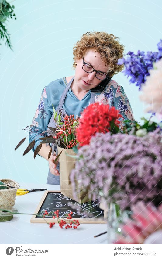 Frau macht Komposition von Blumen im Laden Blumenhändler Werkstatt Blumenstrauß Ordnung Smartphone reden multitask Floristik Handwerk Papier Tasche Tüte