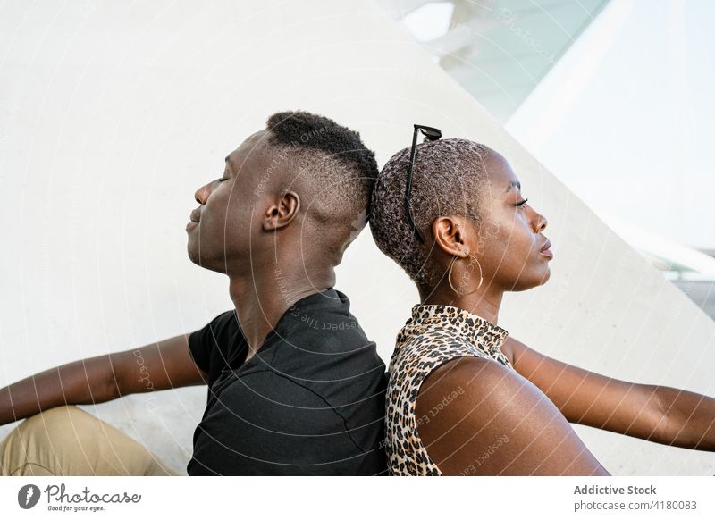 Schwarze Freunde sitzen Rücken an Rücken in der Stadt Zusammensein Straße cool Kurze Haare Vorschein trendy jung urban ethnisch schwarz Afroamerikaner ruhen