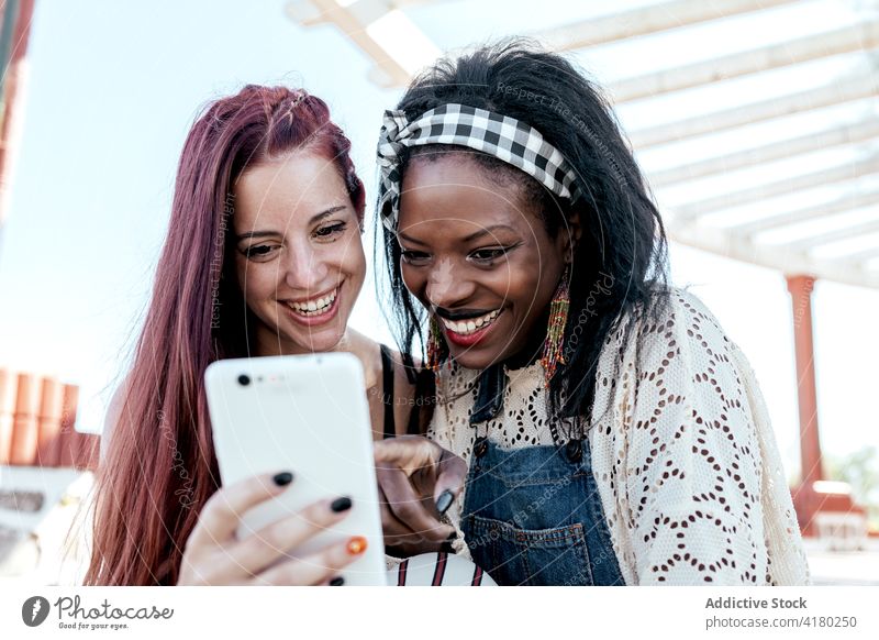 Fröhliche multiethnische Freundinnen, die am Strand gemeinsam ihr Smartphone benutzen lesbisch benutzend Zusammensein heiter Umarmung Paar Telefon Mobile Glück