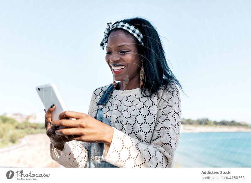 Glückliche schwarze Frau mit Smartphone am Strand benutzend heiter Browsen Mobile Telefon jung Apparatur Gerät Lifestyle ethnisch Afroamerikaner Lächeln online