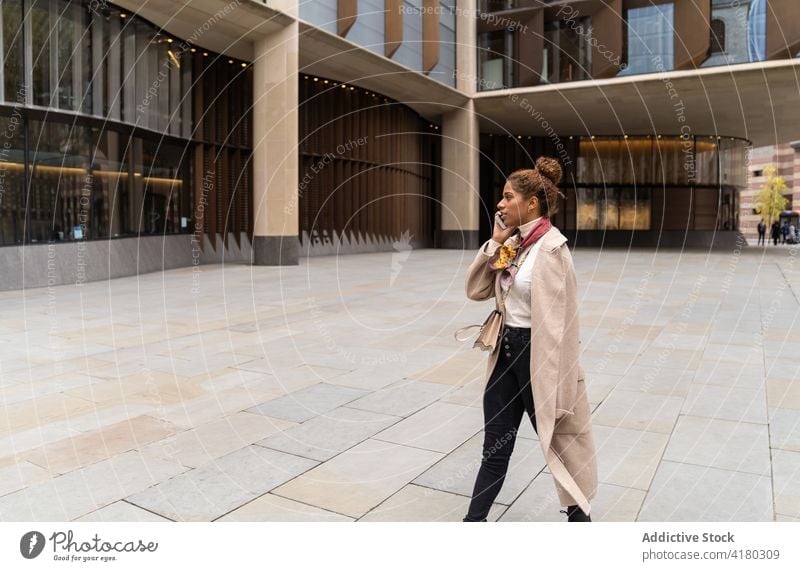 Junge Afroamerikanerin, die in der Stadt spazieren geht und mit ihrem Smartphone spricht Frau Spaziergang Telefonanruf Großstadt Quadrat Gespräch beschäftigt
