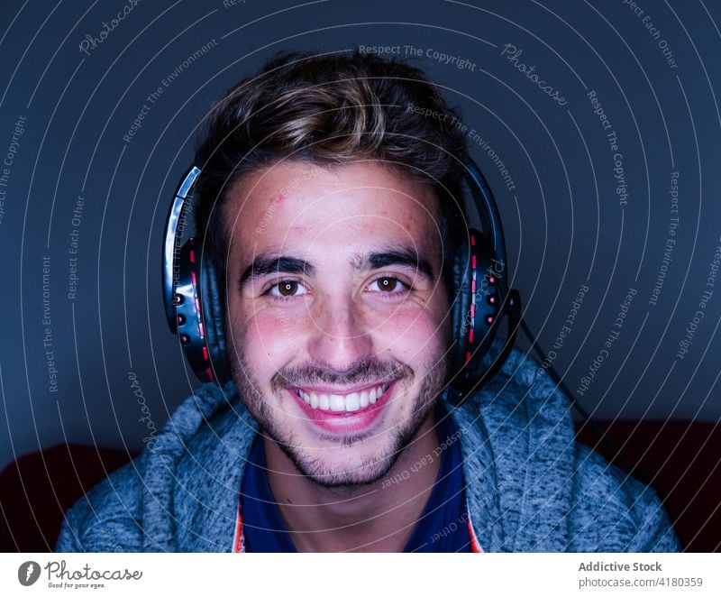 Fröhlicher Mann mit Headset sitzt am Schreibtisch mit Computer Glück Zahnfarbenes Lächeln anlehnen heiter Kopfhörer Arbeit Apparatur dunkel benutzend