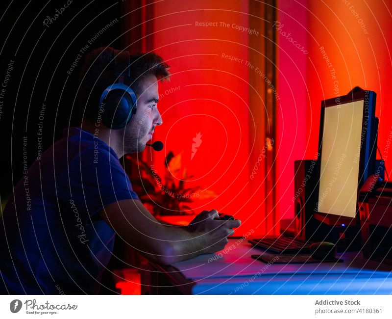 Mann mit Kopfhörern an einem modernen Computer in einem dunklen Raum benutzend Monitor Browsen Dunkelheit Apparatur Windstille Arbeit leerer Bildschirm