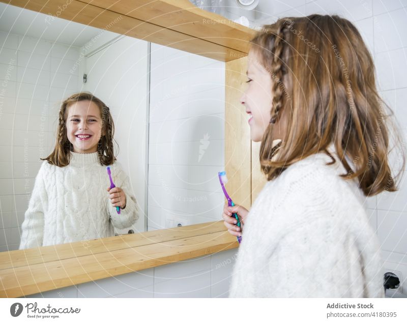 Fröhliches Mädchen beim Zähneputzen und Blick in den Spiegel Bad Zahnbürste Zahnfarbenes Lächeln Glück Freude heiter Hygiene Routine täglich positiv modern