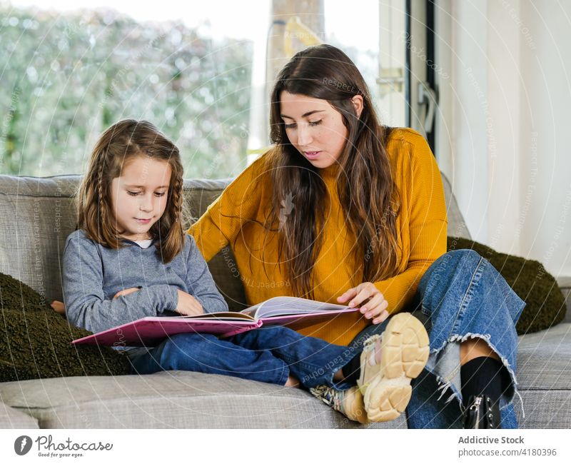 Teenager mit Schwester beim Lesen eines Buches auf dem Sofa im Haus lesen Punkt Zeit verbringen interagieren Wochenende Lächeln heimwärts Zeitvertreib Inhalt