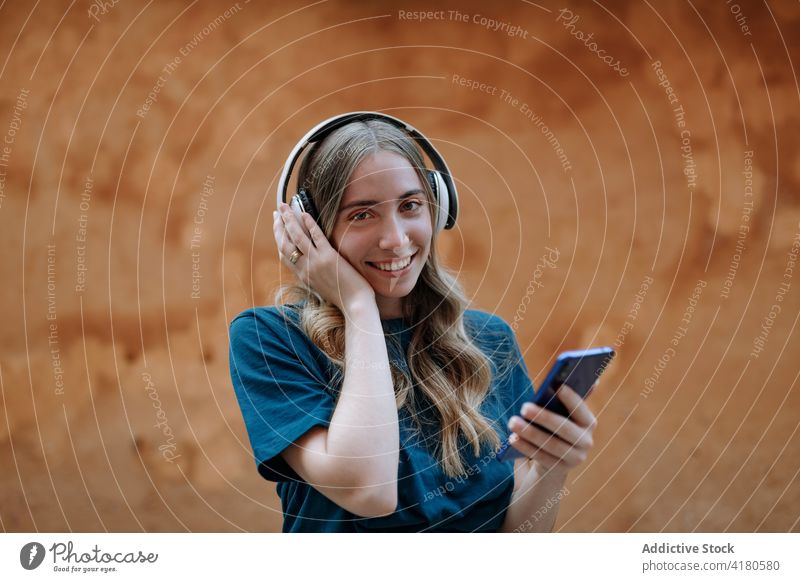Aufmerksame Frau mit Kopfhörern, die auf der Straße mit ihrem Smartphone chattet Textnachrichten Internet Stadt benutzend Apparatur Gerät Headset plaudernd