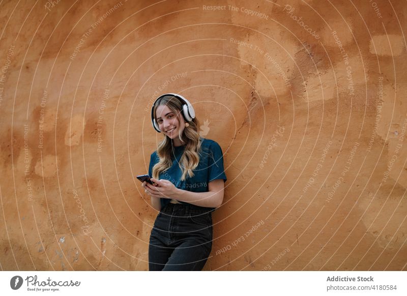 Aufmerksame Frau mit Kopfhörern, die auf der Straße mit ihrem Smartphone chattet Textnachrichten Headset zuhören Musik Internet Stadt benutzend Apparatur Gerät