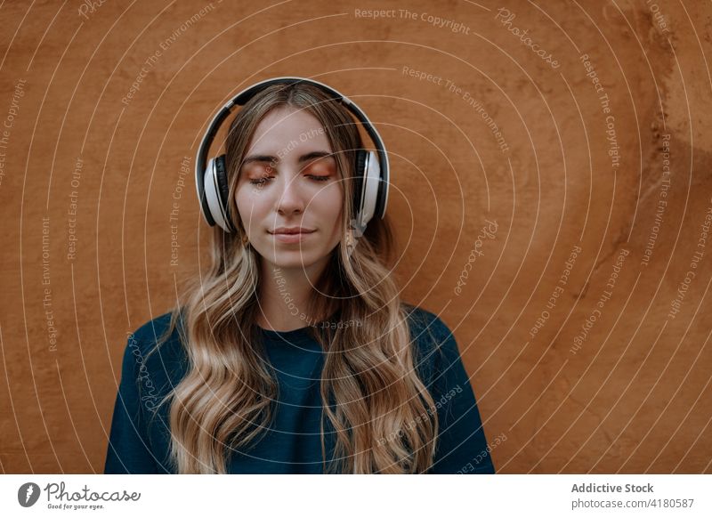 Verträumte Frau, die in der Stadt mit Kopfhörern Musik hört zuhören Gesang Augen geschlossen nachdenklich genießen verträumt Drahtlos benutzend Apparatur Straße
