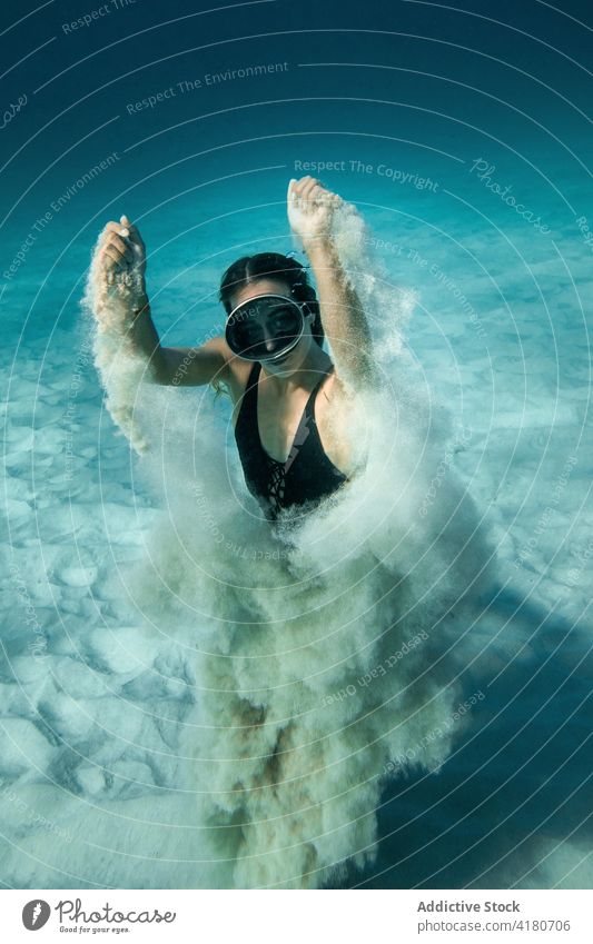 Frau mit Schwimmbrille schwimmt unter Wasser und schaut in die Kamera MEER schwimmen Sinkflug Schutzbrille Sand unterseeisch Badeanzug Taucher schlank Anmut