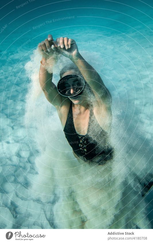 Frau mit Schwimmbrille schwimmt unter Wasser und schaut in die Kamera MEER schwimmen Sinkflug Schutzbrille Sand unterseeisch Badeanzug Taucher schlank Anmut