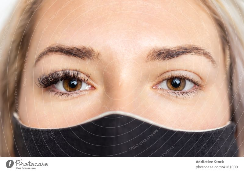 Crop-Frau in Maske mit Wimpernverlängerung an einem Auge künstlich Verlängerung Kosmetologie Windstille Schönheit Mundschutz Coronavirus braunes Auge Blick