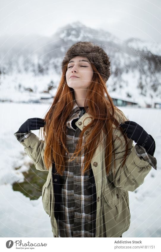 Verträumter Reisender in Oberbekleidung vor verschneitem Berg Augen geschlossen atmen genießen Berge u. Gebirge Schnee Harmonie idyllisch Winter Frau Ornament