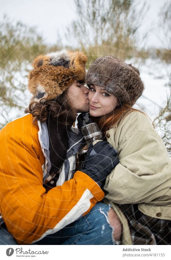 Paar in Pelzmützen umarmt gegen verschneiten Berg Umarmen Liebe Partnerschaft Zeit verbringen Wochenende Tourismus Schnee Winter Harmonie Berge u. Gebirge Fell