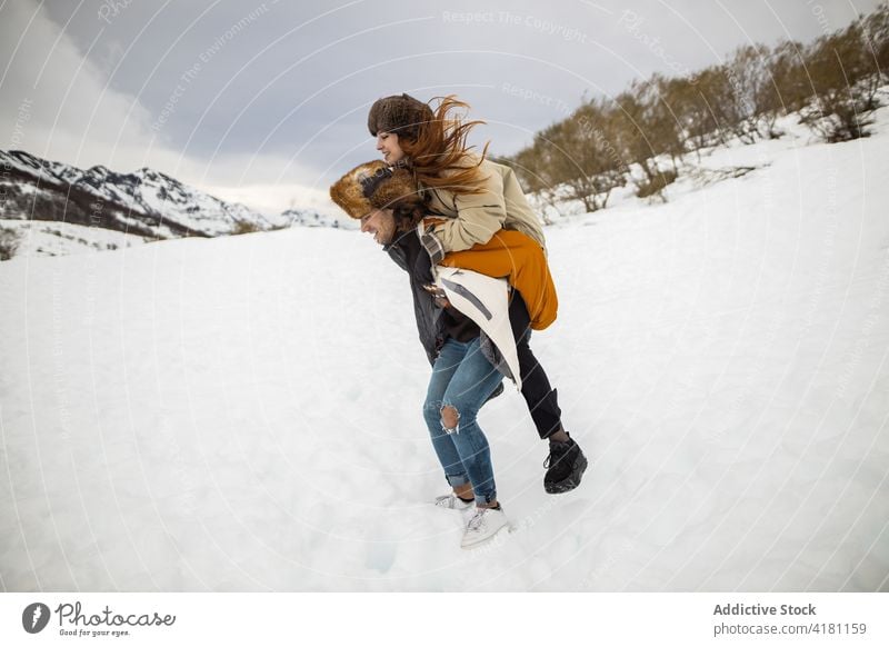 Glückliche Frau, die während eines Winterausflugs huckepack auf ihrem Freund reitet Huckepack Mitfahrgelegenheit Freundin Freiheit Spaß haben Schnee Reittier