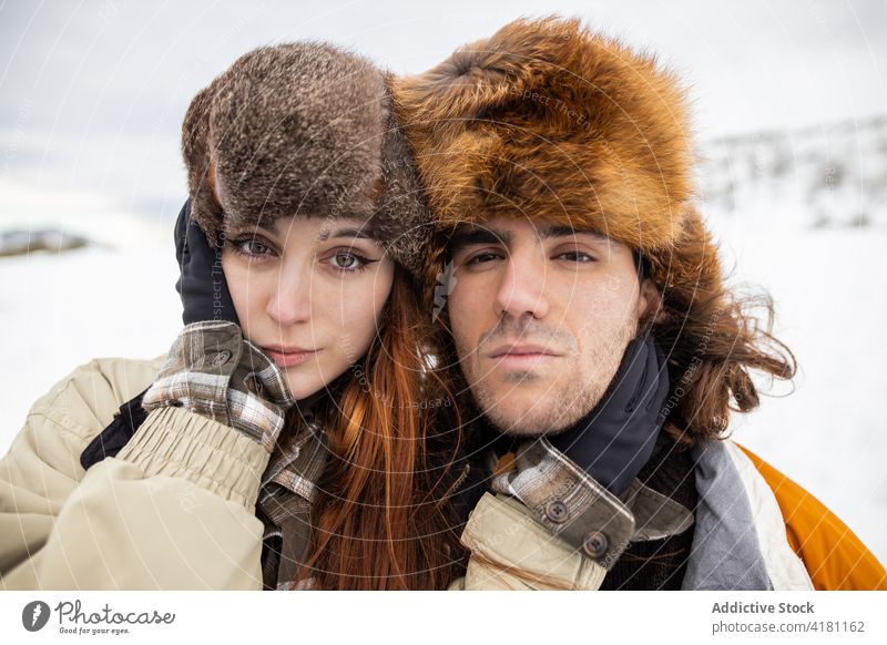 Paar in Pelzmützen umarmt gegen verschneiten Berg Umarmen Liebe Partnerschaft Zeit verbringen Wochenende Tourismus Schnee Winter Porträt Harmonie