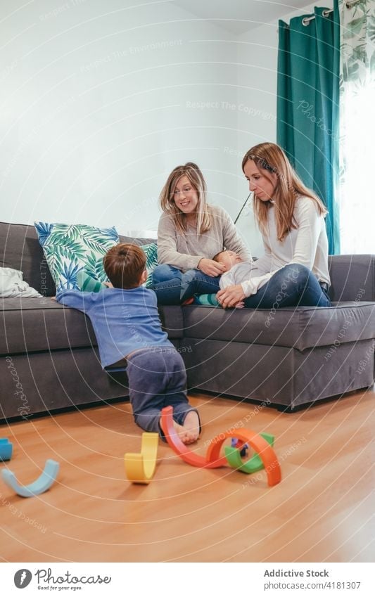 Glückliches lesbisches Paar auf Sofa mit Blick auf spielenden Sohn Familie heiter Mutter alternativ lgbtq Freude zu Hause Homosexualität bezaubernd