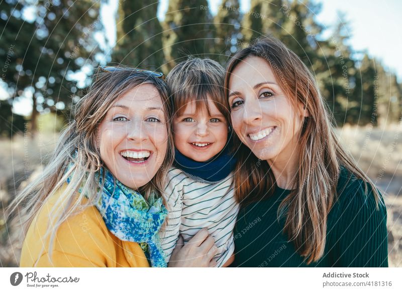 Lächelndes lesbisches Paar, das sich mit seinem Sohn in der Natur umarmt Umarmung Zahnfarbenes Lächeln Umarmen Familie Freude lgbt Zeit verbringen heiter
