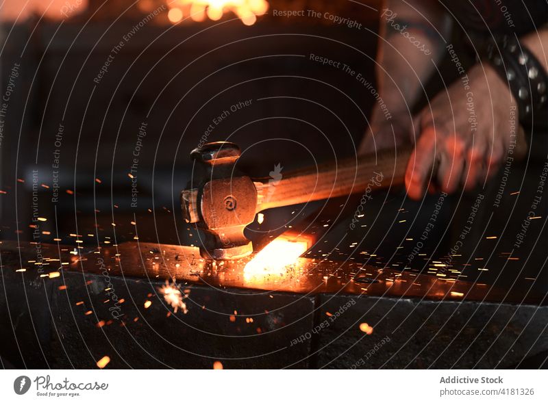 Fokussierter junger Schmied beim Erhitzen und Schlagen von Metall auf dem Amboss in der Werkstatt Mann Hufschmied Treffer bügeln Schmiede Funken manuell Hammer