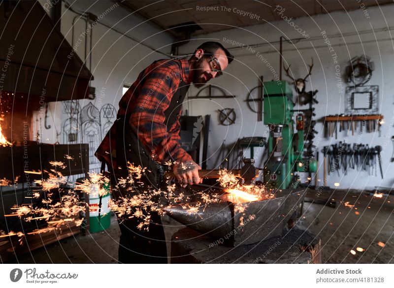 Fokussierter junger Schmied beim Erhitzen und Schlagen von Metall auf dem Amboss in der Werkstatt Mann Hufschmied Treffer bügeln Schmiede Funken manuell Hammer