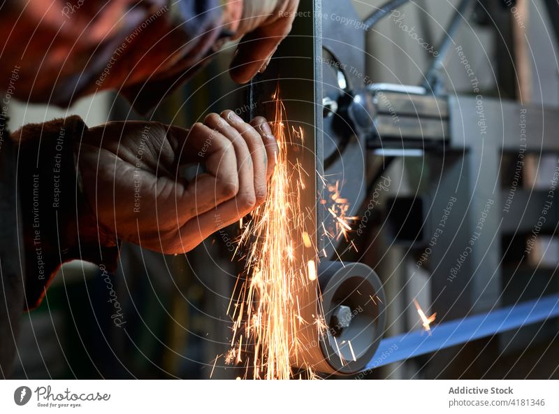 Unbekannter männlicher Schmied, der ein Eisenteil von Hand mit einer Maschine in einer Schmiede schleift Mann polnisch Schleifmaschine Metallbearbeitung
