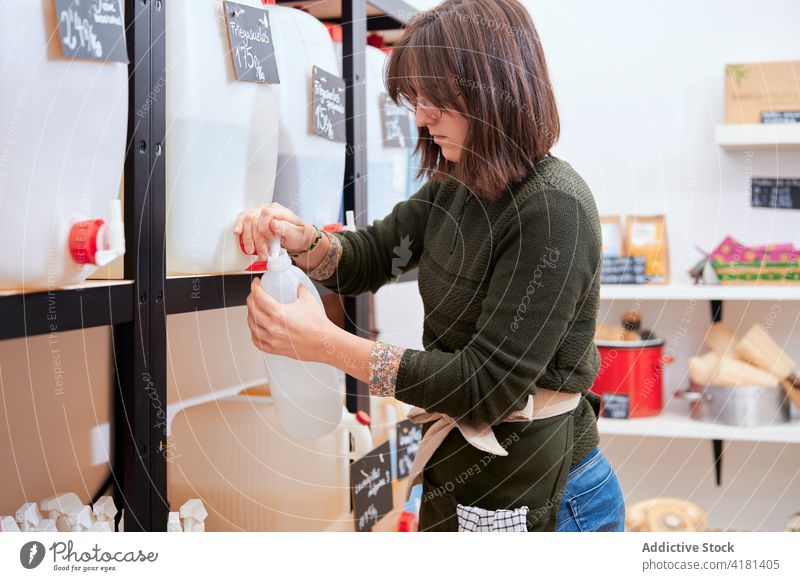 Junge Frau gießt Öko-Reinigungsmittel in eine Flasche eingießen Spülmittel Chemikalie Vermittler nachhaltig Laden Wasserhahn Verkäufer Arbeit