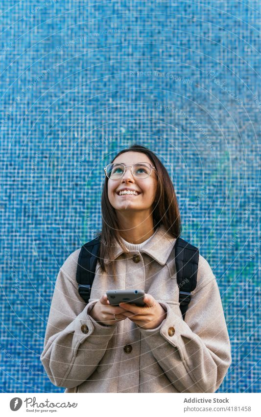 Fröhliche Frau, die auf der Straße ihr Smartphone durchsucht Schüler benutzend Browsen Zahnfarbenes Lächeln Rucksack Arbeitsweg urban Glück Surfen schön