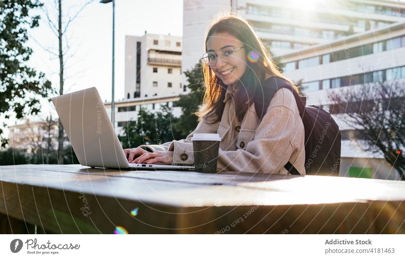 Fröhliche Studentin bei der Arbeit am Laptop im Stadtpark Frau Schüler Zahnfarbenes Lächeln Park Anweisung heiter benutzend Campus Apparatur Pause Kaffee