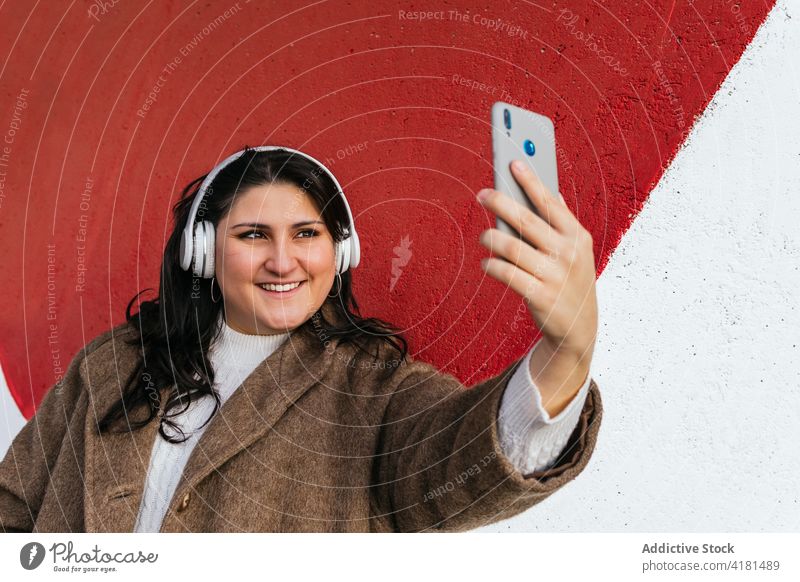 Lächelnde Frau mit Headset, die ein Selfie mit ihrem Smartphone im Freien macht Moment Gedächtnis Kopfhörer zuhören Musik heiter benutzend Apparatur Drahtlos