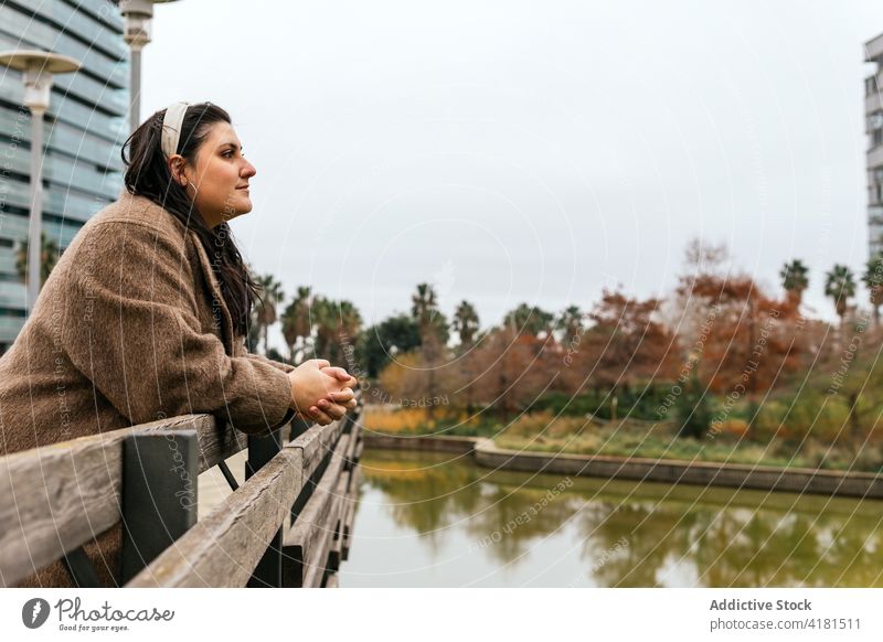 Verträumte Frau genießt Teich von eingezäunten Böschung im Herbst Stadt bewundern Natur verträumt Hände gefaltet reflektieren Großstadt Zaun idyllisch