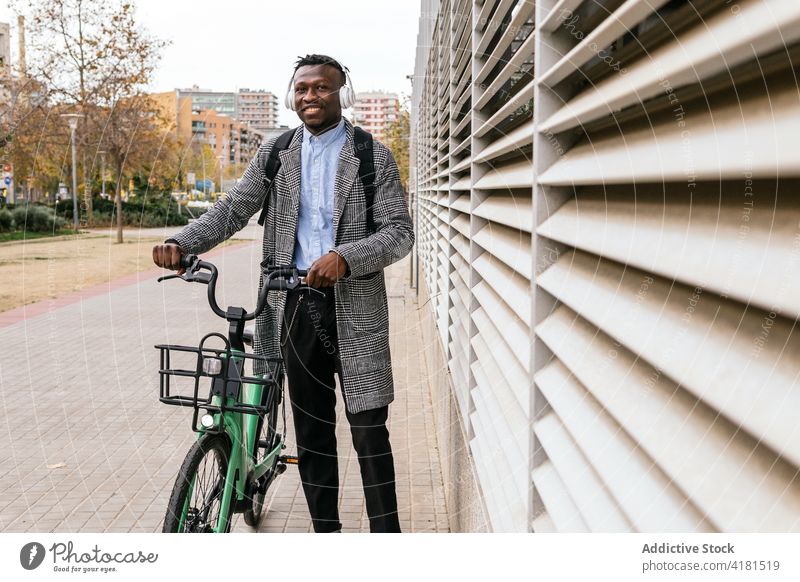 Fröhlicher schwarzer Büroangestellter mit Fahrrad auf einer Stadtstraße Mann heiter formal Stil Fahrzeug Straßenbelag freundlich Afroamerikaner Wand gerippt