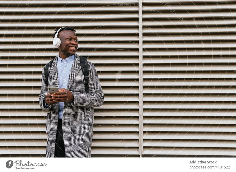 Glücklicher schwarzer Büroangestellter, der mit seinem Smartphone in der Nähe der Wand plaudert Mann Arbeiter Textnachrichten Fahrrad Lächeln Internet Headset