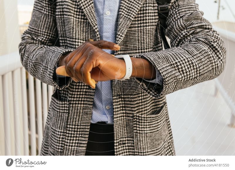 Schwarzer Geschäftsmann, der auf einer Brücke die Zeit auf seiner Smartwatch überprüft zuschauend intelligente Uhr punktuell Zeitmanagement modern Stil