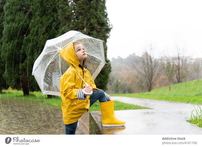 Nettes Kind unter Regenschirm an einem regnerischen Tag im Herbst Park gelb Regenmantel nass Wetter ruhig wasserdicht Gummi Stiefel feucht fallen Stil Kindheit