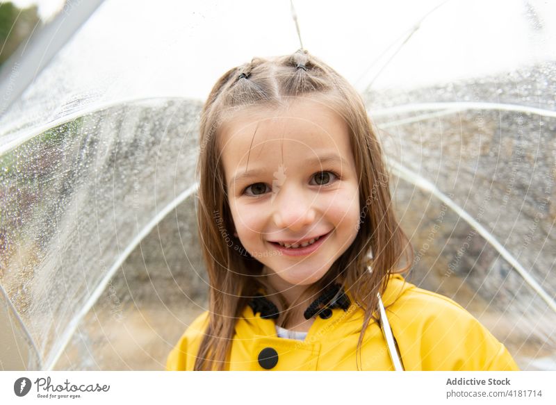 Lächelndes Mädchen unter Regenschirm an einem regnerischen Tag Kind Regenmantel heiter nass Wassertropfen gelb durchsichtig Kindheit Wetter charmant Vergnügen