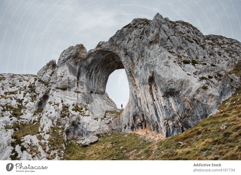 Entfernter Reisender in natürlichem Felsbogen stehend Felsen Golfloch Bogen erkunden Berge u. Gebirge Formation wolkig Fernweh Natur Asturien Spanien Abenteuer