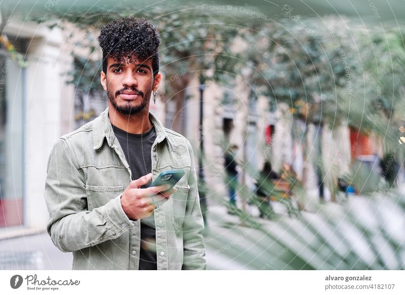 ein junger hipsanischer Mann, der sein Mobiltelefon an einem bewölkten Tag im Freien benutzt Mitteilung Telefon Glück Technik & Technologie männlich Latein