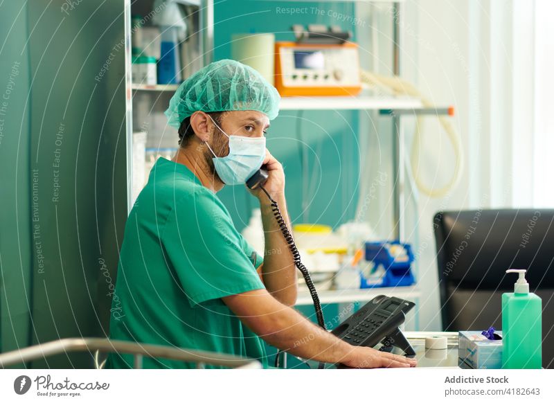 Fokussierter Pfleger am Telefon in der Klinik Mann reden Krankenhaus Konzentration Sanitäter beschäftigt diskutieren Station Gesundheitswesen Arzt männlich jung
