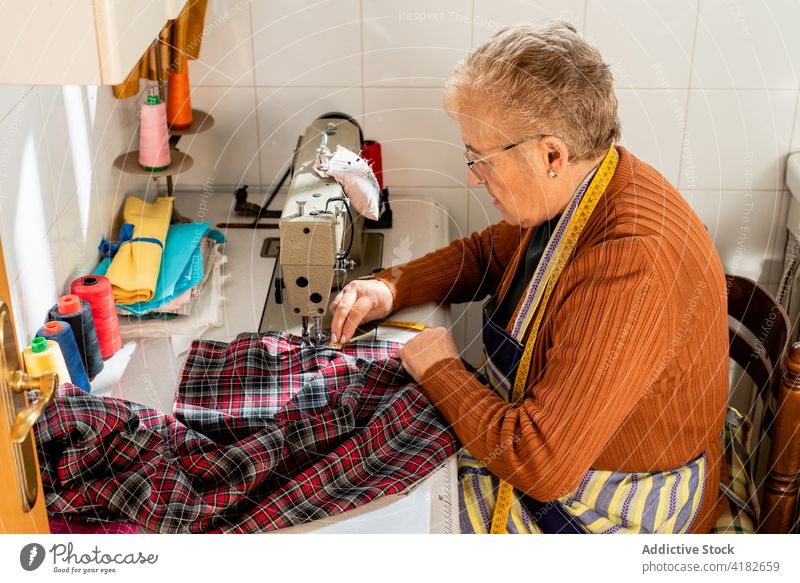 Konzentrierte ältere Schneiderin beim Nähen von Kleidung in der Werkstatt Frau Näherin nähen Stoff Faser sticken Abwasserkanal Senior Damenschneiderin
